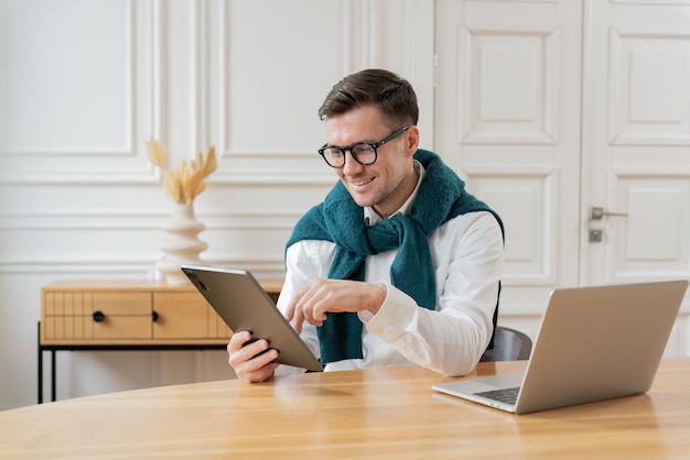 Foto un hombre enfocado con gafas y una bufanda azul azul revisa una tableta de pie en un elegante espacio de oficina