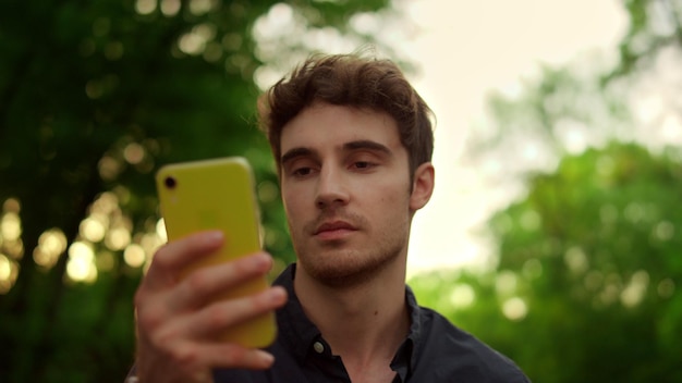 Hombre enfocado en el primer plano usando un teléfono inteligente al aire libre al atardecer Retrato de un hombre serio leyendo un mensaje en línea en el teléfono móvil durante una caminata en el parque