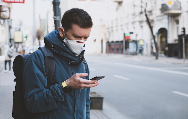 Hombre enmascarado en la calle con un teléfono inteligente