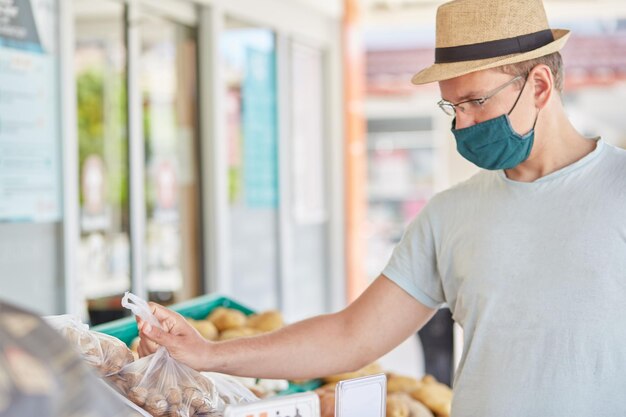 Hombre enmascarado compra verduras en un mercado de granjeros callejeros Concepto de cuarentena de coronavirus Foto de alta calidad