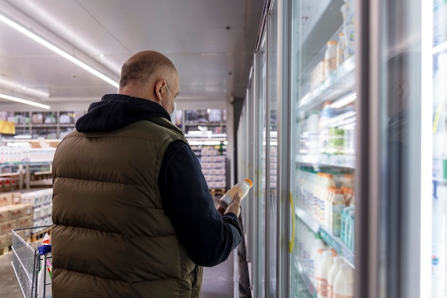 Un hombre enmascarado en la sección de productos lácteos de un supermercado. Vista trasera. Pandemia de coronavirus.