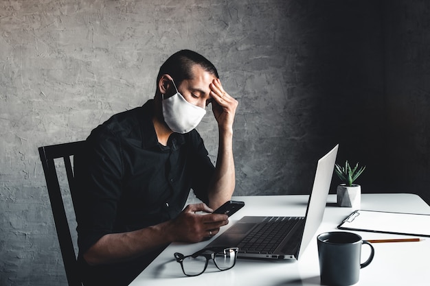 Un hombre enmascarado trabaja en una computadora. Pandemia, coronavirus, epidemia