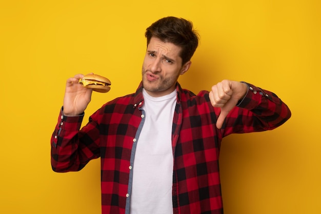 Hombre enojado que sostiene la hamburguesa que muestra los pulgares hacia abajo