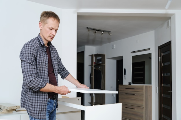 El hombre ensambla los muebles en casa coloca la parte superior de la cómoda