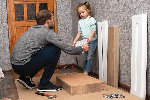 un hombre ensambla muebles en casa con sus propias manos y su pequeña hija lo ayuda