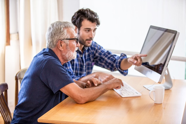 Hombre enseñando a anciano a usar la computadora