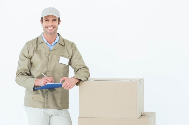 Hombre de entrega feliz escribiendo en portapapeles por cajas de cartón