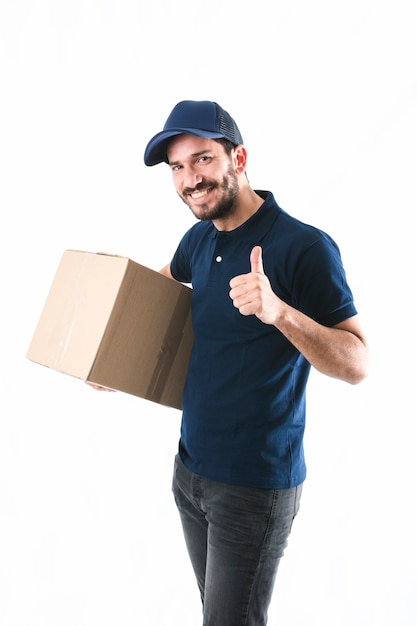 Hombre de entrega feliz que sostiene la caja de cartón que muestra el pulgar para arriba en el fondo blanco