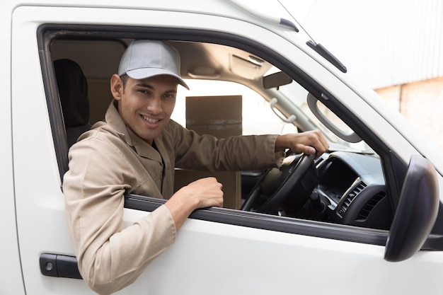 Foto hombre de entrega mirando a la cámara mientras está sentado en el asiento delantero del coche fuera del almacén