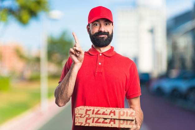 Hombre de entrega de pizza apuntando hacia arriba en el fondo desenfocado
