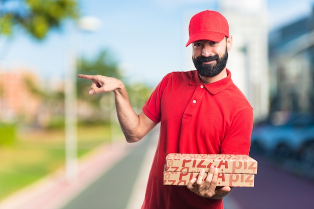 Hombre de entrega de pizza apuntando a la lateral sobre fondo desenfocado