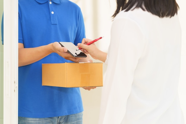 Hombre de entrega señalando en el teléfono inteligente y la mujer que recibe el paquete