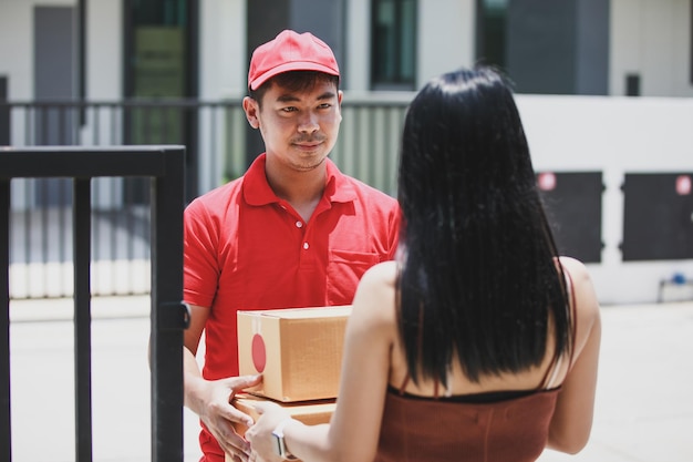 Foto hombre de entrega sosteniendo una caja de cartón mientras una hermosa mujer joven pone su firma en el portapapeles