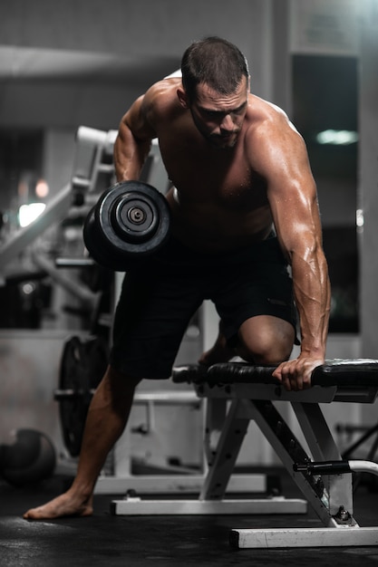 Hombre entrena en el gimnasio. Hombre atlético entrena con mancuernas, bombeando sus bíceps.