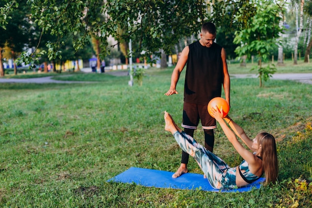 Hombre entrenador enseñando a una mujer a hacer ejercicio con una pelota