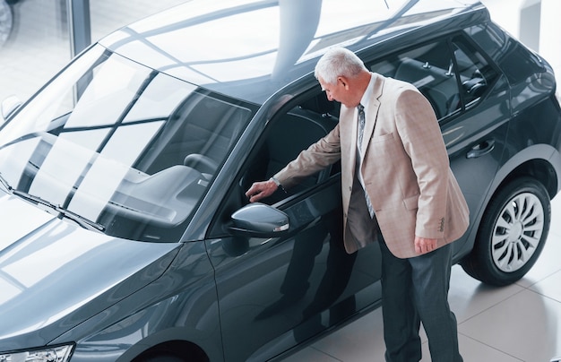 Hombre envejecido en ropa formal caminando en el salón del automóvil y buscando el coche.