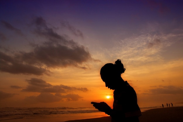 Hombre enviando mensajes de texto con smartphone en la playa durante la puesta de sol