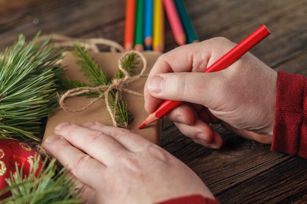 Hombre envuelto a mano regalo de Navidad en el papel sobre la mesa de madera oscura, vista superior