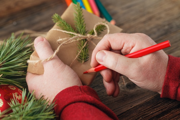 Foto hombre envuelto a mano regalo de navidad en el papel sobre la mesa de madera oscura, vista superior