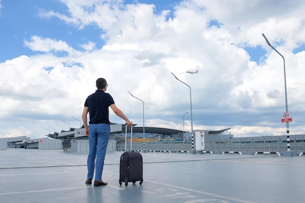 Un hombre con equipaje de viaje en el aeropuerto en el estacionamiento mira al cielo