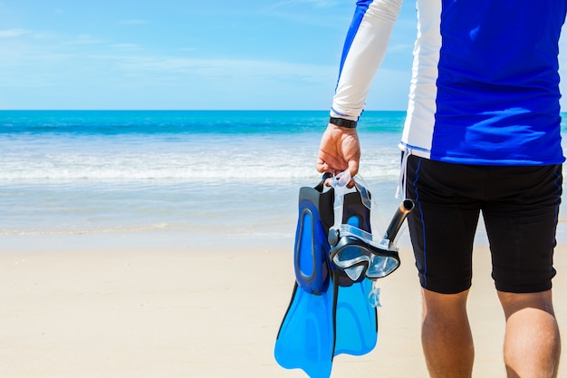 Hombre con equipo de snorkel en manos yendo al mar en la playa