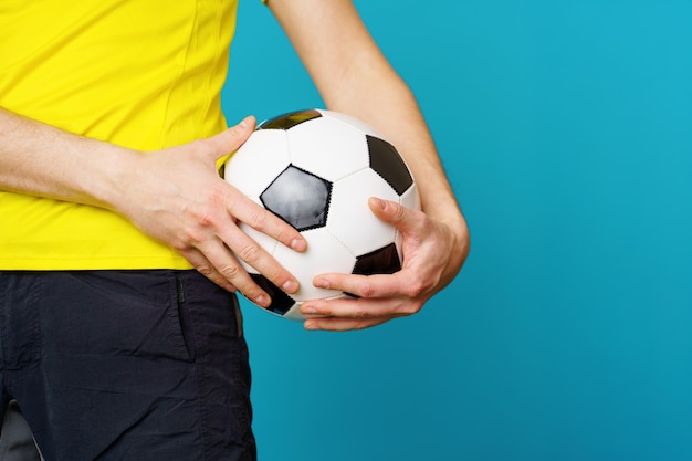 El hombre es fan de fútbol en camiseta amarilla con balón de fútbol sobre fondo azul.