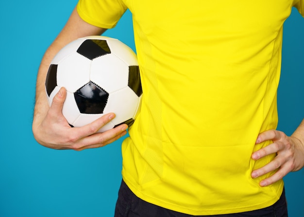 Foto el hombre es fan de fútbol en camiseta amarilla con balón de fútbol sobre fondo azul.