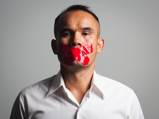 El hombre es silenciado con cinta adhesiva roja en la boca sellada para evitar que hable. Concepto de libertad