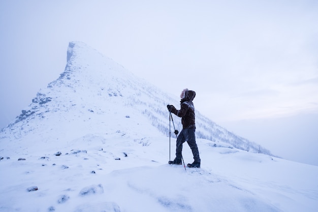 Foto hombre escalador con bastones de trekking de pie en la montaña nevada