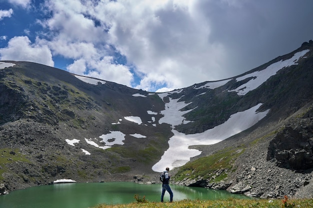 un hombre, un escalador con mochila, sube a la cima de una montaña cerca de un lago azul. Altai
