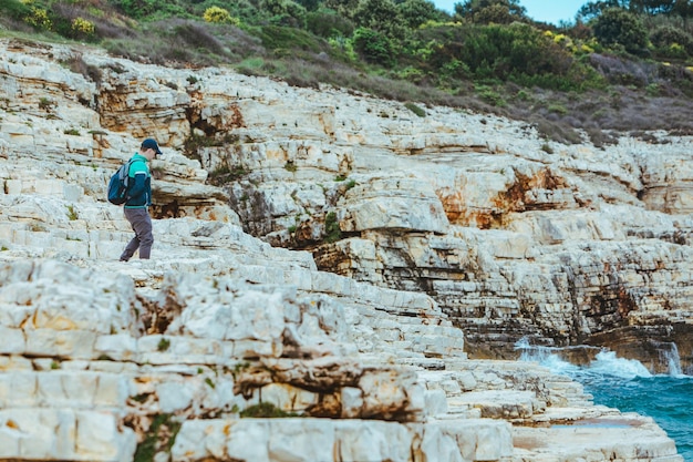 Hombre escalando el borde rocoso disfrutando de la vista del paisaje marino