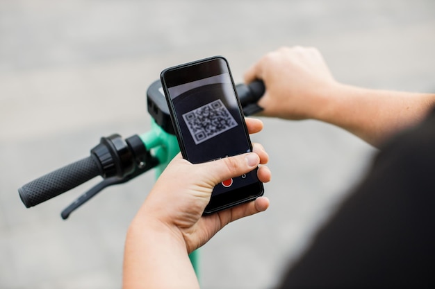 El hombre escanea el código QR por teléfono inteligente para desbloquear y alquilar scooter eléctrico en la calle