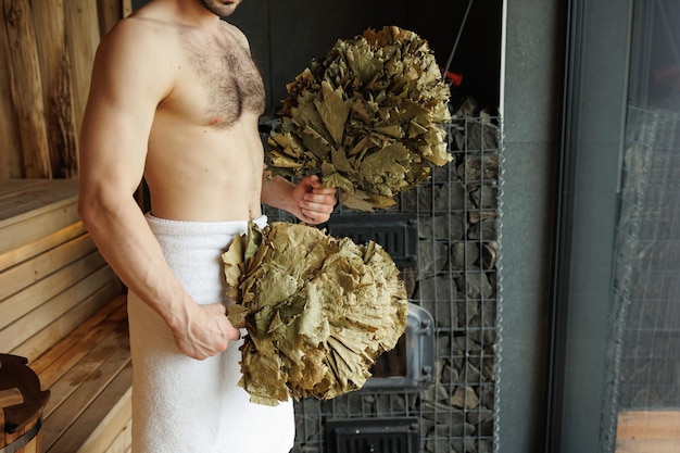 Hombre con una escoba para bañarse en la sauna.