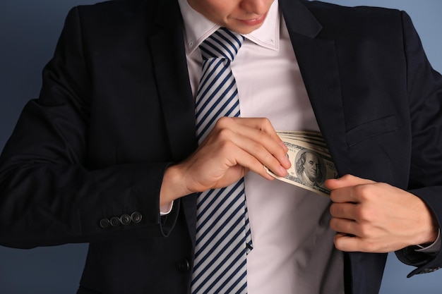 Hombre escondiendo billetes de dólar en traje sobre fondo gris
