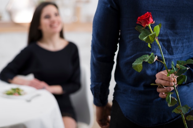 Hombre escondiendo una rosa roja de su novia