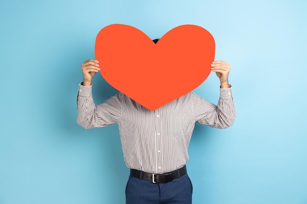 Hombre escondiendo su rostro detrás de un gran corazón de papel leído sosteniendo un símbolo de amor cuidado generosidad dar esperanza