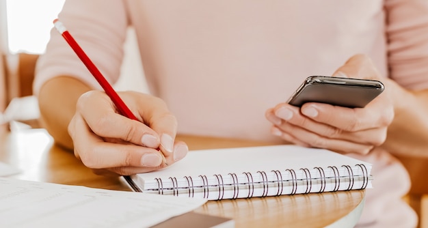 El hombre escribe información empresarial en un cuaderno en el lugar de trabajo en la oficina con el teléfono inteligente