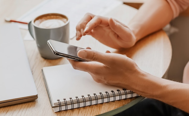 El hombre escribe información empresarial en un cuaderno en el lugar de trabajo en la oficina con el teléfono inteligente