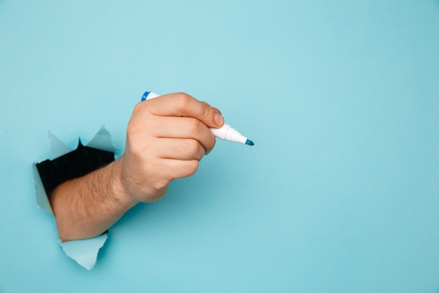 Un hombre escribe un marcador en una pared de papel azul roto