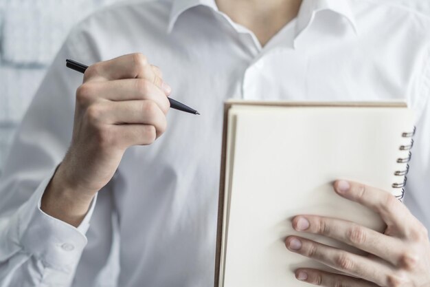 El hombre escribe de pie con un bolígrafo en un cuaderno en una oficina soleada concepto de educación y negocios Cerrar