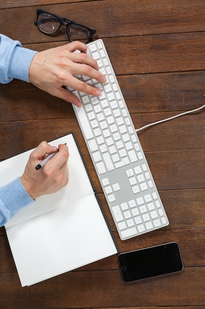 Hombre escribiendo en el teclado y escribiendo en el diario