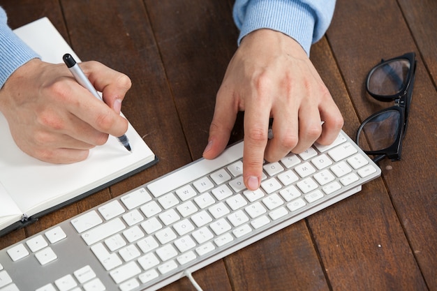 Hombre escribiendo en el teclado y escribiendo en el diario