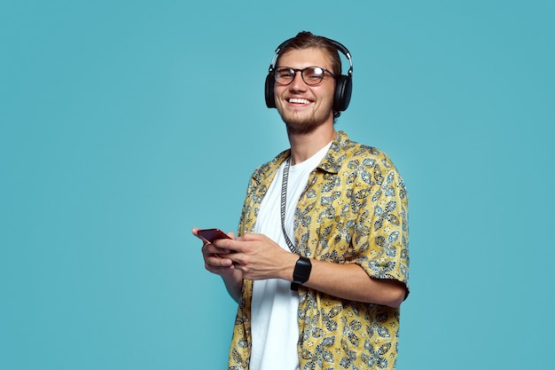 El hombre escucha música con auriculares desde el teléfono móvil contra la pared azul