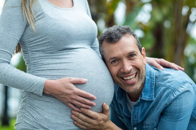 Hombre escuchando el estómago de la mujer embarazada al aire libre