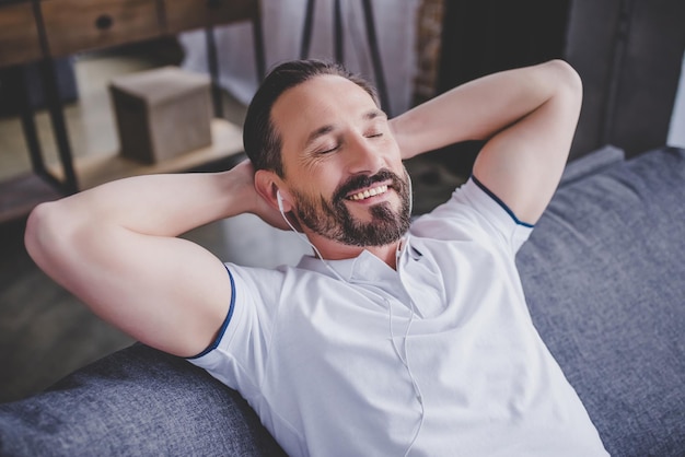 Hombre escuchando música con auriculares y relajándose en el sofá de casa