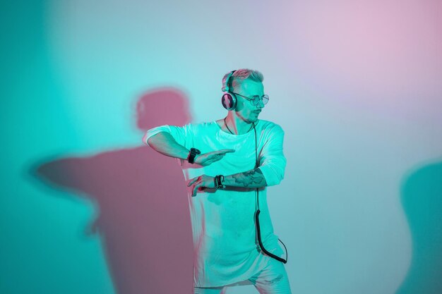 Hombre escuchando música y bailando en estudio con luz rosa y azul creativa