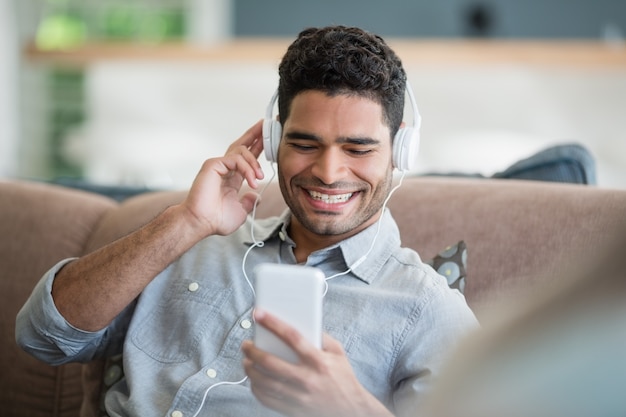 Hombre escuchando música en el teléfono móvil en la sala de estar