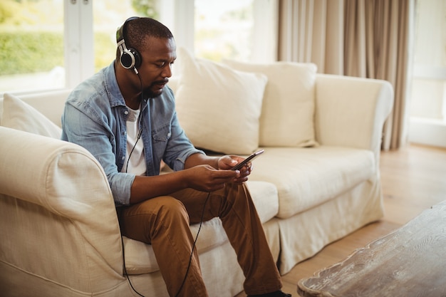 Hombre escuchando música en el teléfono móvil en la sala de estar