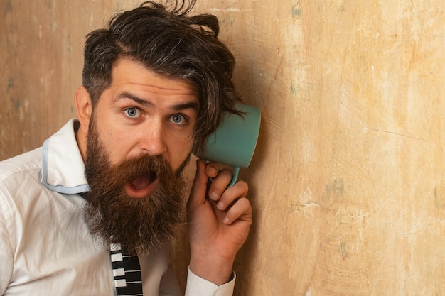 Hombre escuchando a través de la pared con los secretos de la taza y el vecino del concepto de chismes y el ma divertido secreto