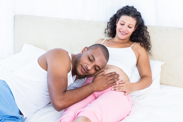 Hombre escuchando el vientre de la feliz esposa embarazada en la cama